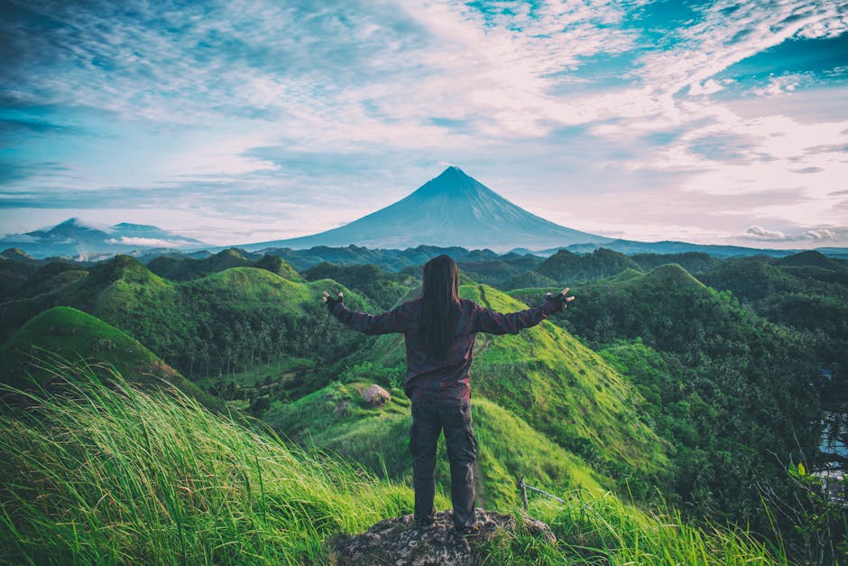 A person enjoys an expansive view of Mt. Mayon amidst lush green hills in Bicol, Philippines